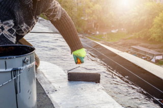 bitu2.jpg Close-up of hand applying roofing sealant at sunset